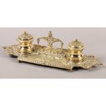 A Victorian brass double desk standish fitted with two glass lined inkwells, pierced handle and