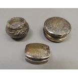 A circular foliate and scroll embossed pill box, another and a rounded rectangular silver pill