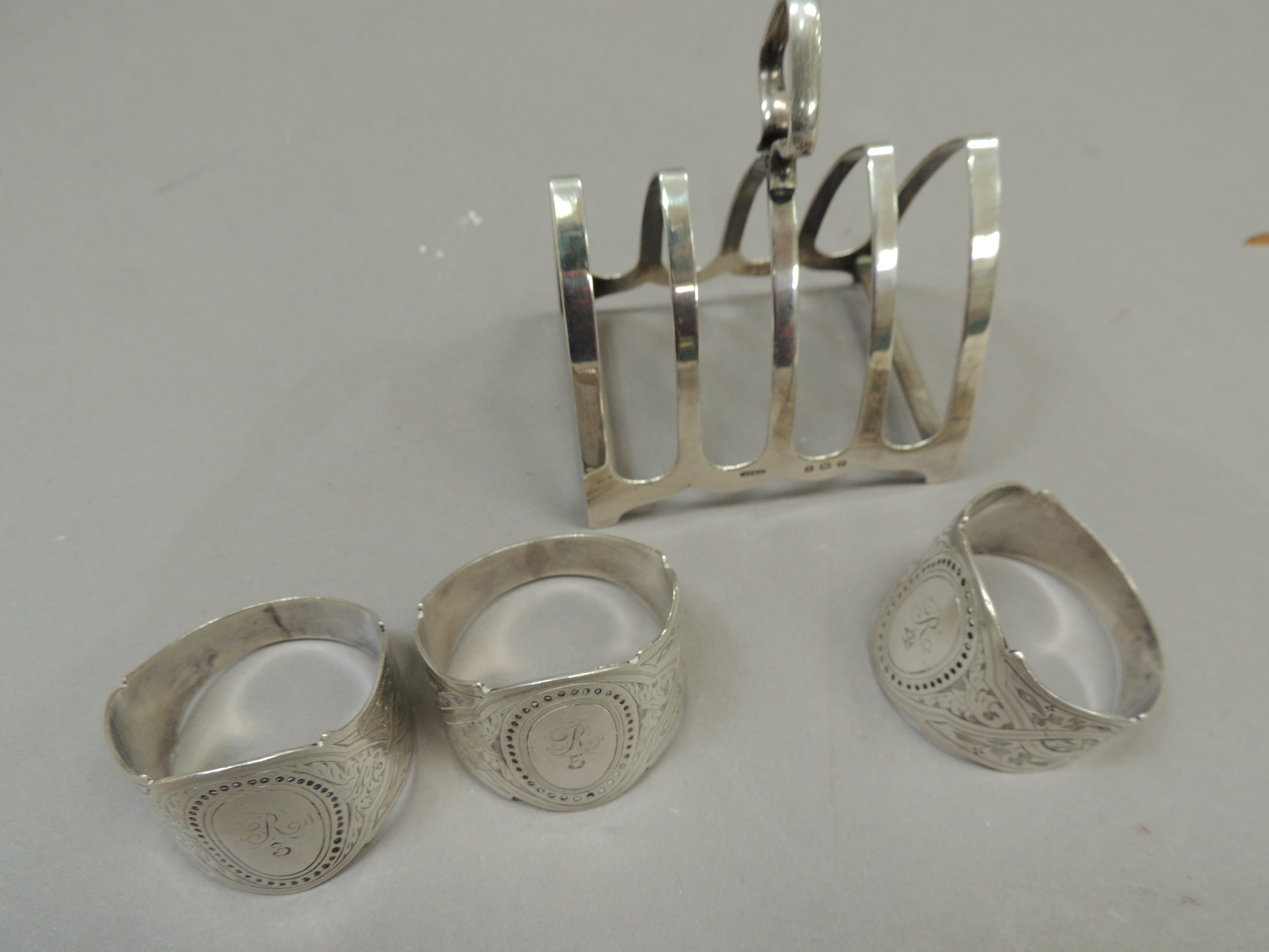 A silver four division toast rack together with three silver napkin rings all initialled 'R',