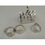 A silver four division toast rack together with three silver napkin rings all initialled 'R',