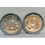 A pair of pottery wall plaques, moulded in relief with figures in a tavern and figures around a