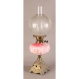 A VICTORIAN BRASS OIL LAMP having a pink glass reservoir moulded with panels of pendant flowers,