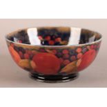 A WILLIAM MOORCROFT POMEGRANATE BOWL tubelined and painted in mauve, ochre and russet on a dark blue