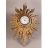 A GILTWOOD STARBURST CLOCK with bead and foliate carved bezel enclosing an enamel dial decorated