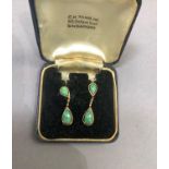 A pair of jade ear pendants, the pear shaped cabochon stones claw set, raised against a surround and