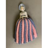 An early 20th century china half doll of a girl wearing a blue bonnet, the lower half knitted pink