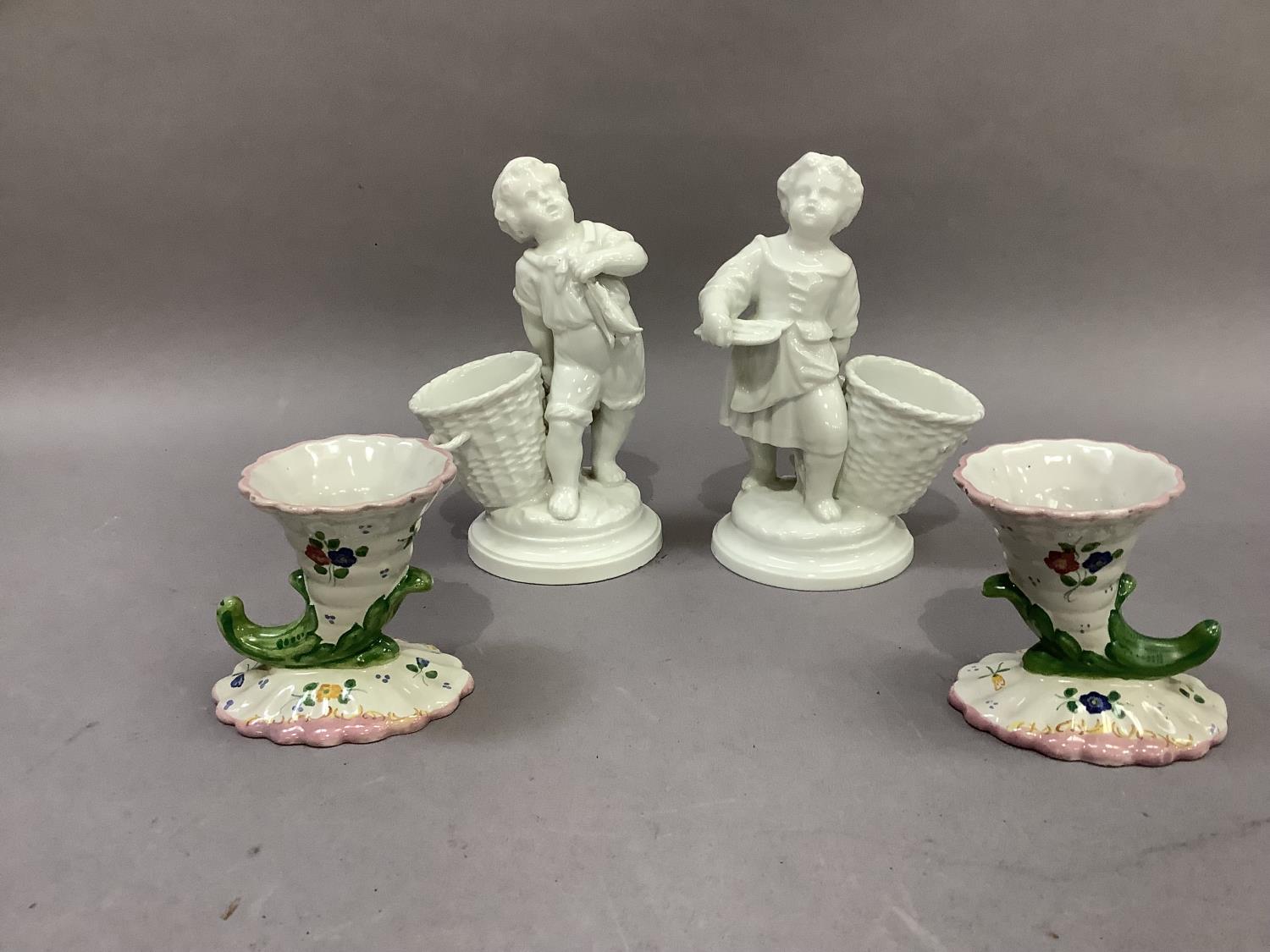 A pair of continental porcelain figures, fisherboys, each standing beside an open basket, 18cm high;