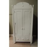 A modern white painted wardrobe with arched top centred on a heart shaped boss flanked by turned