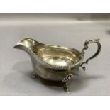 A George V silver sauce boat with gadrooned rim, flying scrolled handle and three shell cast