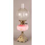 A Victorian brass oil lamp having a pink glass reservoir moulded with panels of pendant flowers,