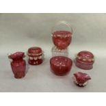 Six items of cranberry glass including two lidded jars with prunt rims together with a jug with