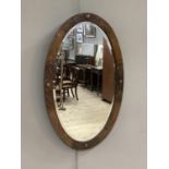 An Edwardian oak framed oval mirror, the frame blind fret carved and with circular buttons to