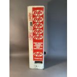 A Kit Kat wall mounted vending machine in red and white, black plastic dispensing handle and