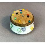 A brass mounted circular enamel pin cushion, ogee form body printed flowers beneath a beaded brass