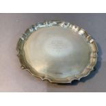 A silver circular salver with pie crust rim, presentation inscription to the centre and on four hoof
