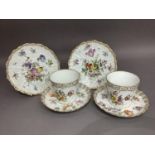 A pair of Dresden china tea cups and saucers wrythern moulded and painted in polychrome enamels with