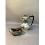 A silver hot water jug of oblong outline with panelled corners, ebonised finial and handle and