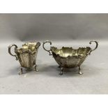 A silver two handled sugar bowl and cream jug of panelled form with C-scroll rim and leaf capped