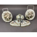A pair of continental china wall plaques mounted in relief with pairs of cherubs together with a