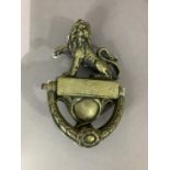 A cast brass door knocker with lion surmount, the canted rectangular top with foliate pendant and