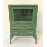 GREEN METAL CABINET with a glass fall door and glass side panels above six small drawers, standing