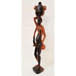 CARVED AFRICAN TEAK FIGURE depicting a man carrying a water container on his head, standing on a