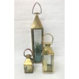 THREE GRADUATED ANTIQUE BRASS EFFECT LANTERNS each with a swing handle and glass panels, 116cm, 67cm