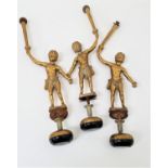 THREE DECORATIVE GILT BRASS PUTTI in loin cloths, with their right arms raised holding a torch, with
