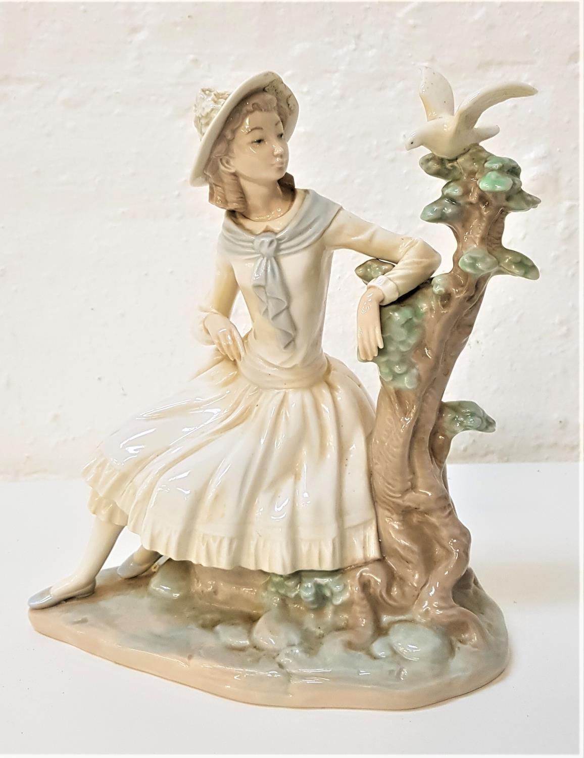 NAO PORCELAIN FIGURINE of a young girl seated by a tree looking at a dove, 24cm high