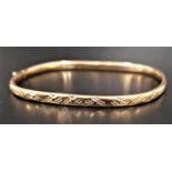 NINE CARAT GOLD BANGLE with engraved detail to one side and with safety clasp, approximately 4.8
