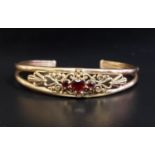 GARNET SET NINE CARAT GOLD BANGLE the three central garnets within decorative pierced scroll