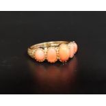 GRADUATED CORAL FIVE STONE RING the five oval cabochon coral sections flanked by scroll and motif