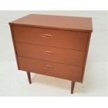 TEAK EFFECT CHEST with three drawers with part inset handles, standing on turned tapering