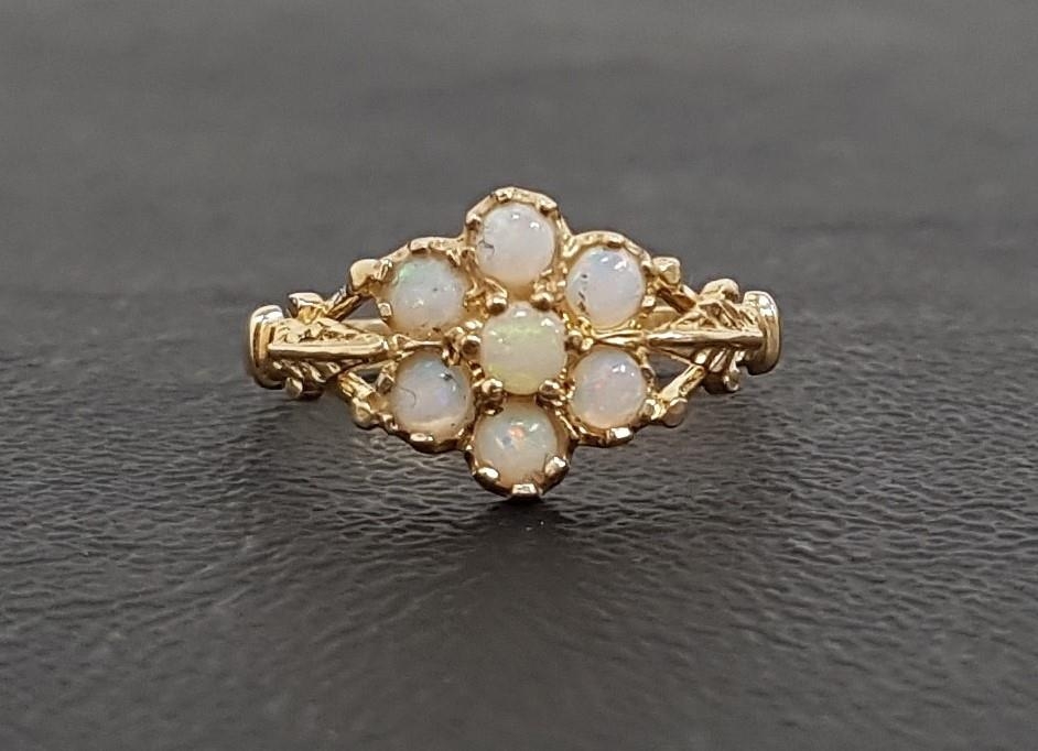 OPAL CLUSTER RING the seven round cabochon opals flanked by shaped and pierced shoulders, on nine