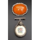 TWO SILVER MOUNTED BROOCHES one with amber coloured oval cabochon within scroll decorated mount; the