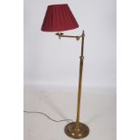 A BRASS FLOOR STANDING READING LAMP with adjustable arm above a cylindrical column on a circular