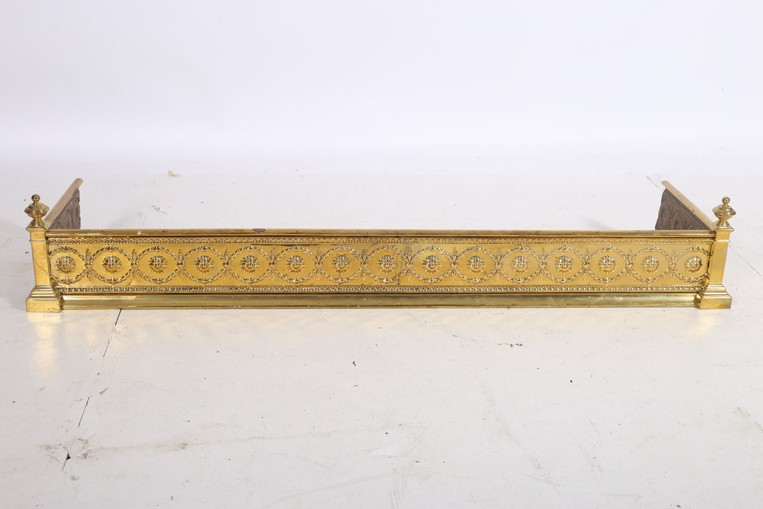 AN ADAMS DESIGN BRASS FENDER with embossed frieze between rectangular columns with urn capitals 21cm