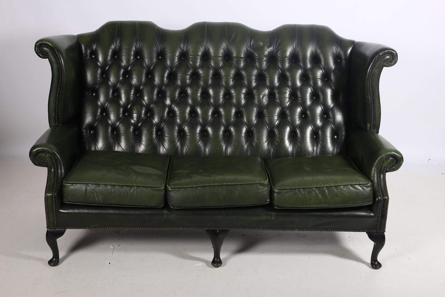 A GREEN HIDE UPHOLSTERED THREE SEATER LIBRARY SETTEE the shaped top rail with deep button