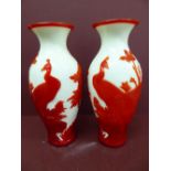 Pair of Chinese red overlay glass vases on a white ground having decoration of peacocks and