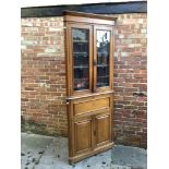 An early 20th century light oak standing corner cupboard in arts and crafts style with a pair of