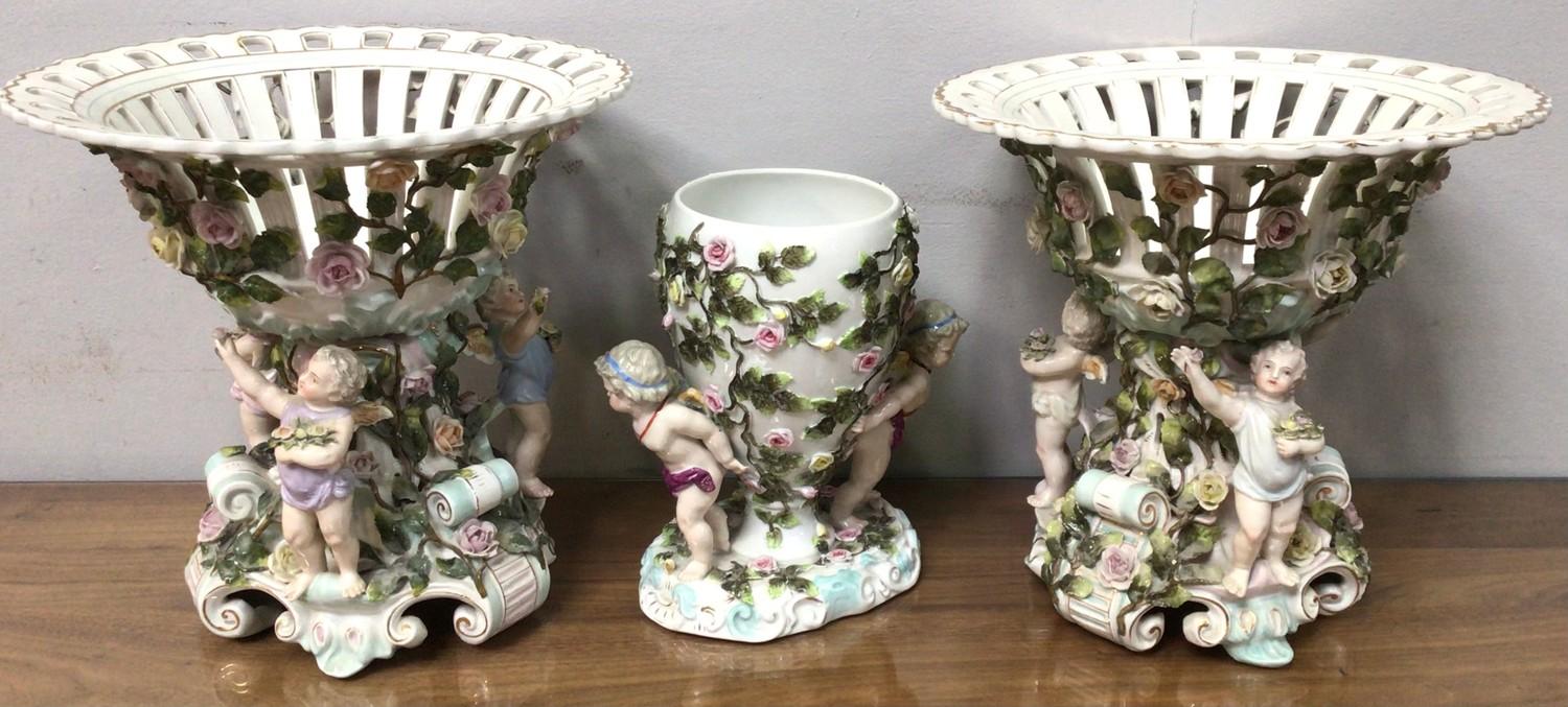 A pair of Sitzendorf figural porcelain comports with pierced bowls, the base with three cherubs