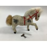 A clockwork toy pony in white with red bridle, natural mane and tail, in working order with key