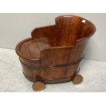 A hard wood child's chair/bath tub, with raised back and removable tray, on wheels, 62cm long