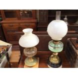 Two various Victorian oil lamps with clear glass reservoirs and white glass shades, raised on