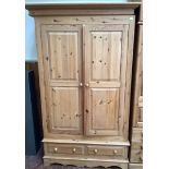 A pine wardrobe, the shaped cornice above a pair of panelled doors enclosing hanging space, over two