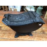 A Victorian black painted cast iron coal scuttle with dished foliate cover, raised on ornately