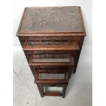 A nest of four Malaysian hardwood tables, each top carved with scenes of figures, buildings and