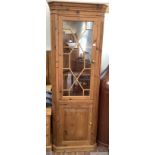 A pine standing corner cabinet, the shaped cornice with dentil moulding, above a glazed door