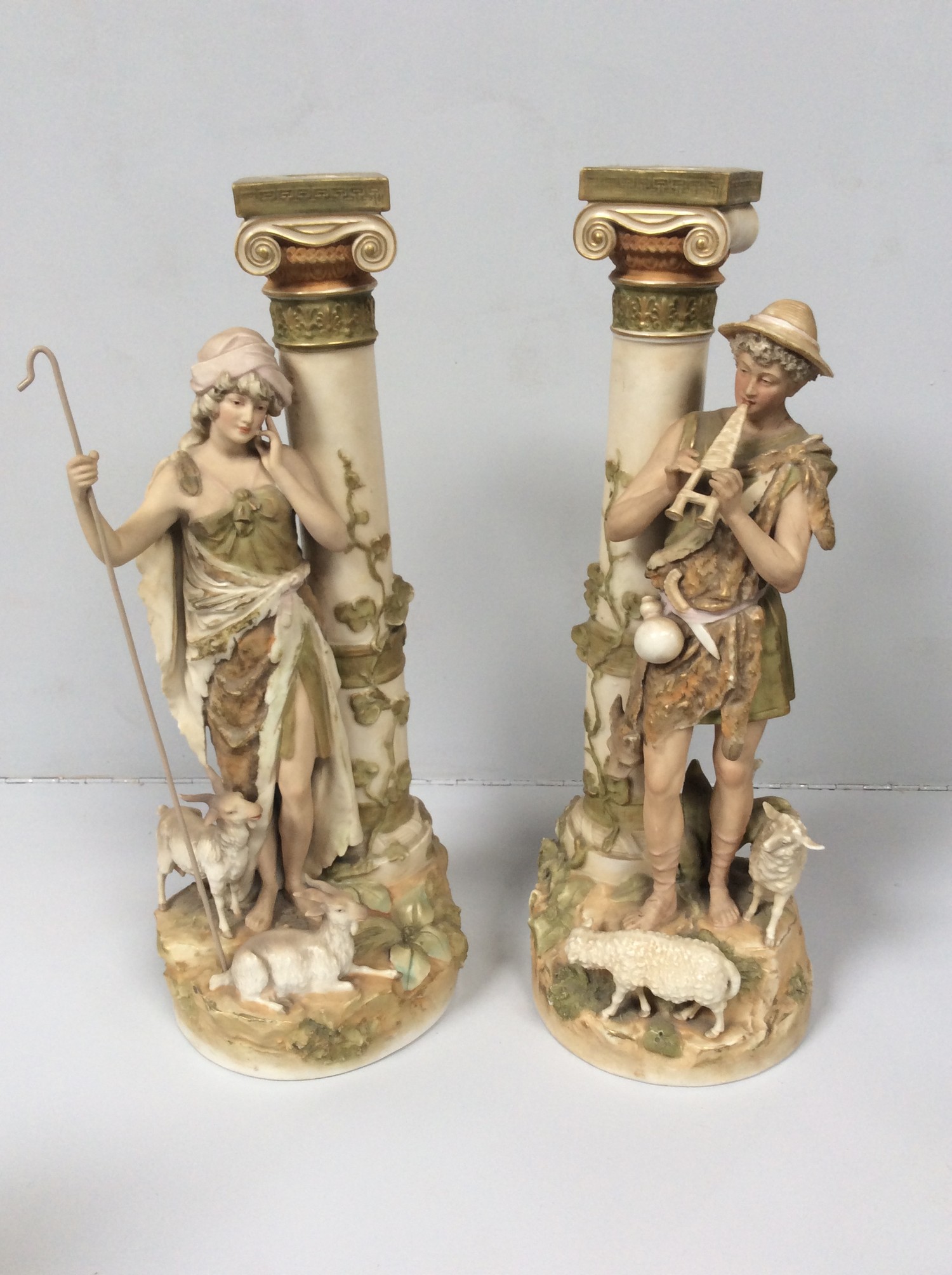 A pair of Royal Dux porcelain figures of a shepherd and shepherdess modelled next to classical Ionic