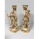 A pair of Royal Dux porcelain figures of a shepherd and shepherdess modelled next to classical Ionic